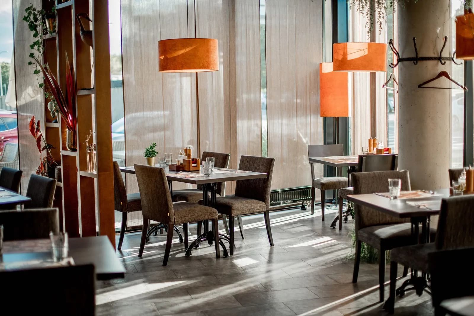 Restaurant tables beside a window wall under orange pendant lamps