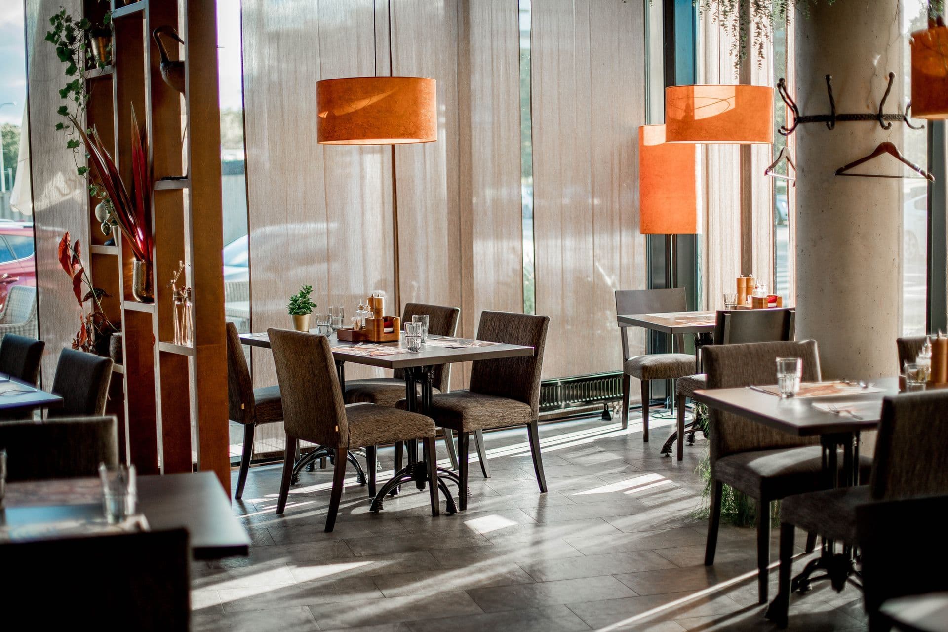 Restaurant tables beside a window wall under orange pendant lamps